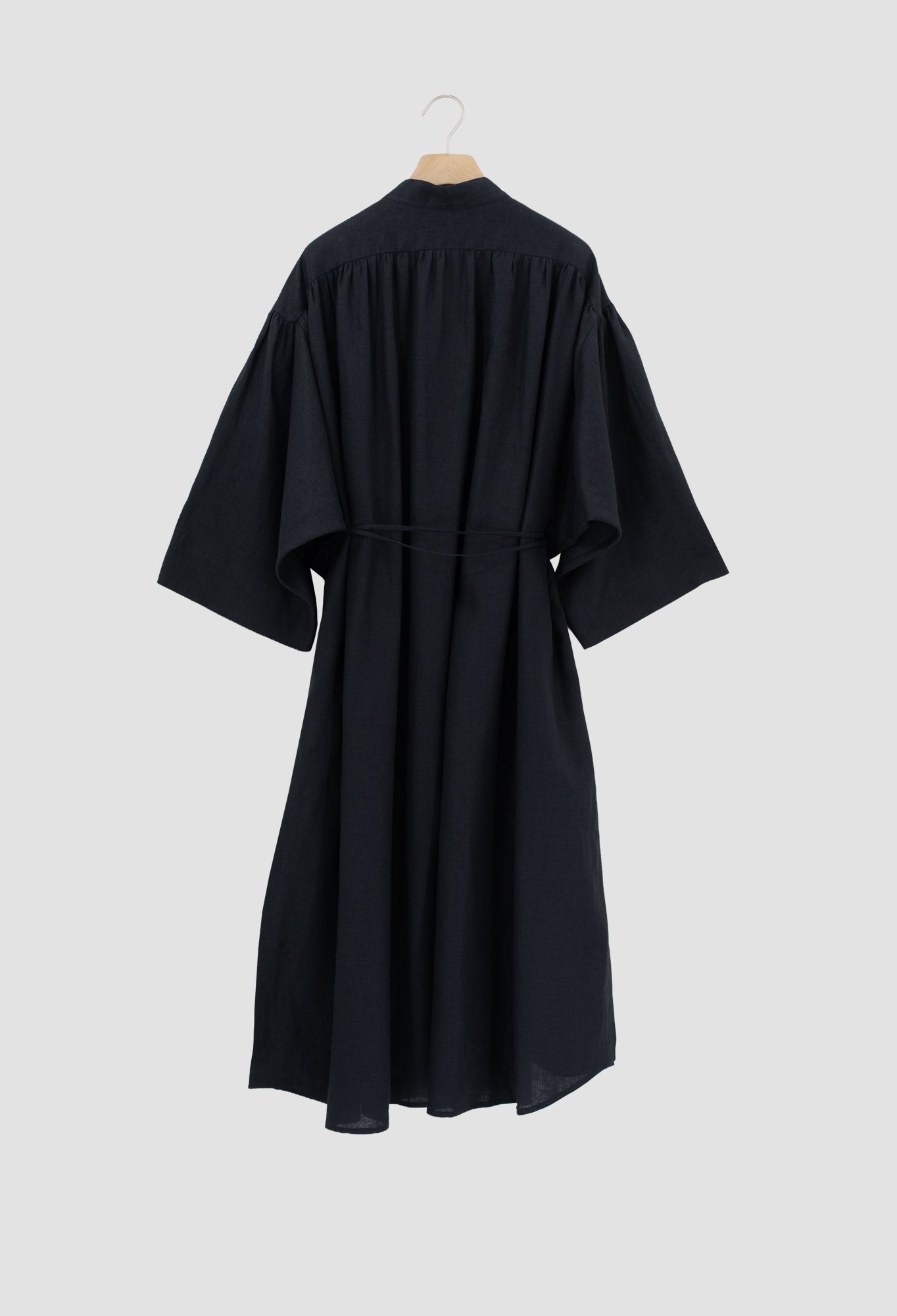 A black kimono-style dress with wide three-quarter sleeves and a self-tie waist belt, shown from the back on a wooden hanger against a light gray background.