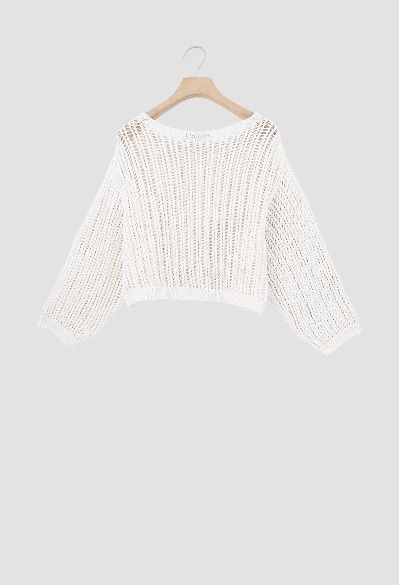 An off-white open-knit cropped sweater with three-quarter sleeves, hanging on a wooden hanger against a solid light gray background.