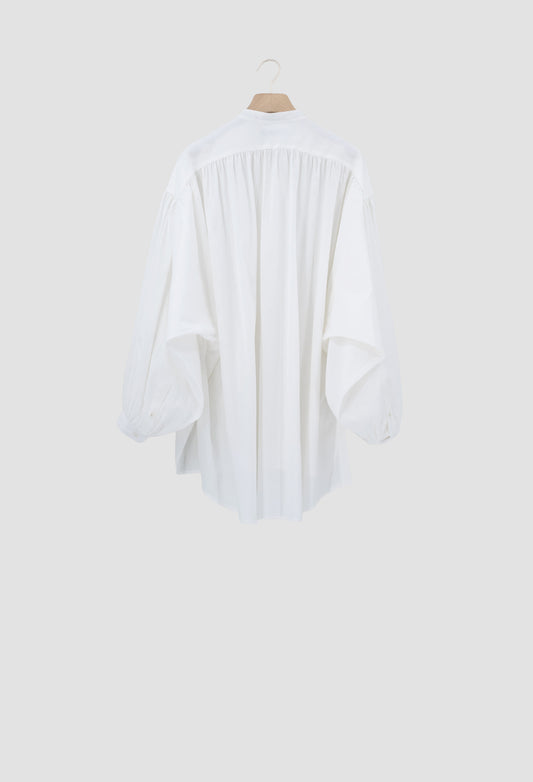A white long-sleeve blouse with a gathered, pleated back detail, hanging on a wooden hanger against a light gray background.