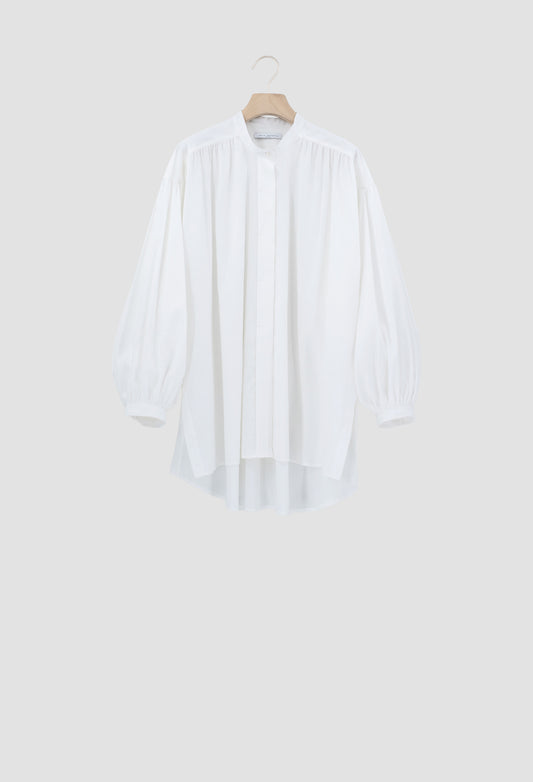 A white long-sleeve blouse with a high-low hem and gathered sleeves, hanging on a wooden hanger against a light gray background.