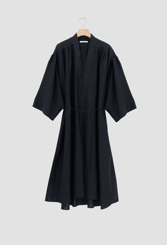 A black wrap-style dress with wide three-quarter sleeves and a self-tie waist belt, hanging on a wooden hanger against a solid light gray background.