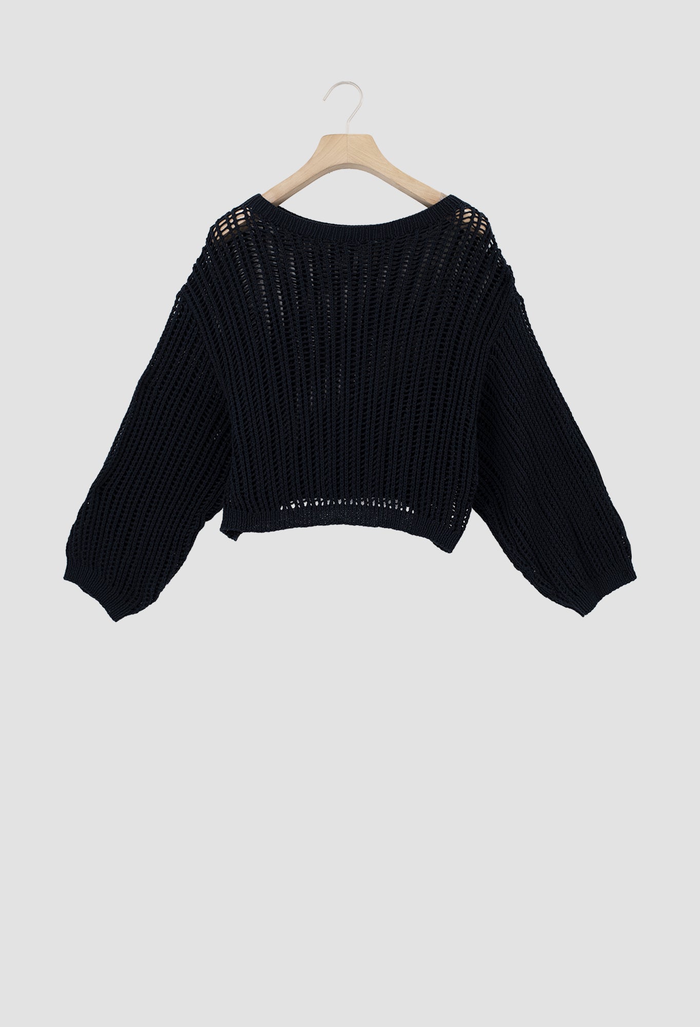 A black ribbed knit cropped sweater with long balloon sleeves and openwork shoulder detailing, hanging on a wooden hanger against a light gray background.