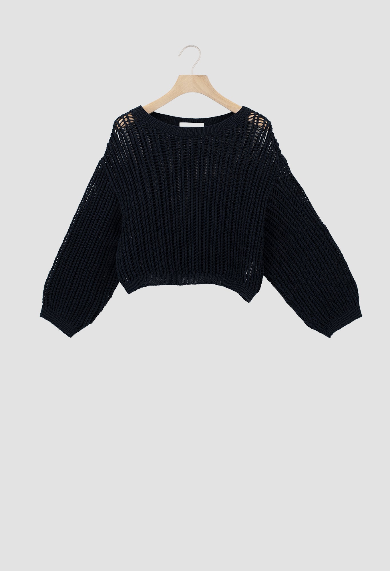 A black open-knit cropped sweater with long sleeves, hanging on a wooden hanger against a light gray background.