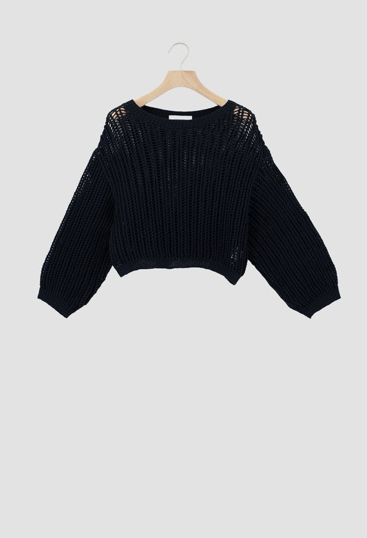 A black open-knit cropped sweater with long sleeves, hanging on a wooden hanger against a light gray background.