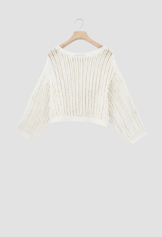 An off-white open-knit cropped sweater with long sleeves, hanging on a wooden hanger against a solid light gray background.