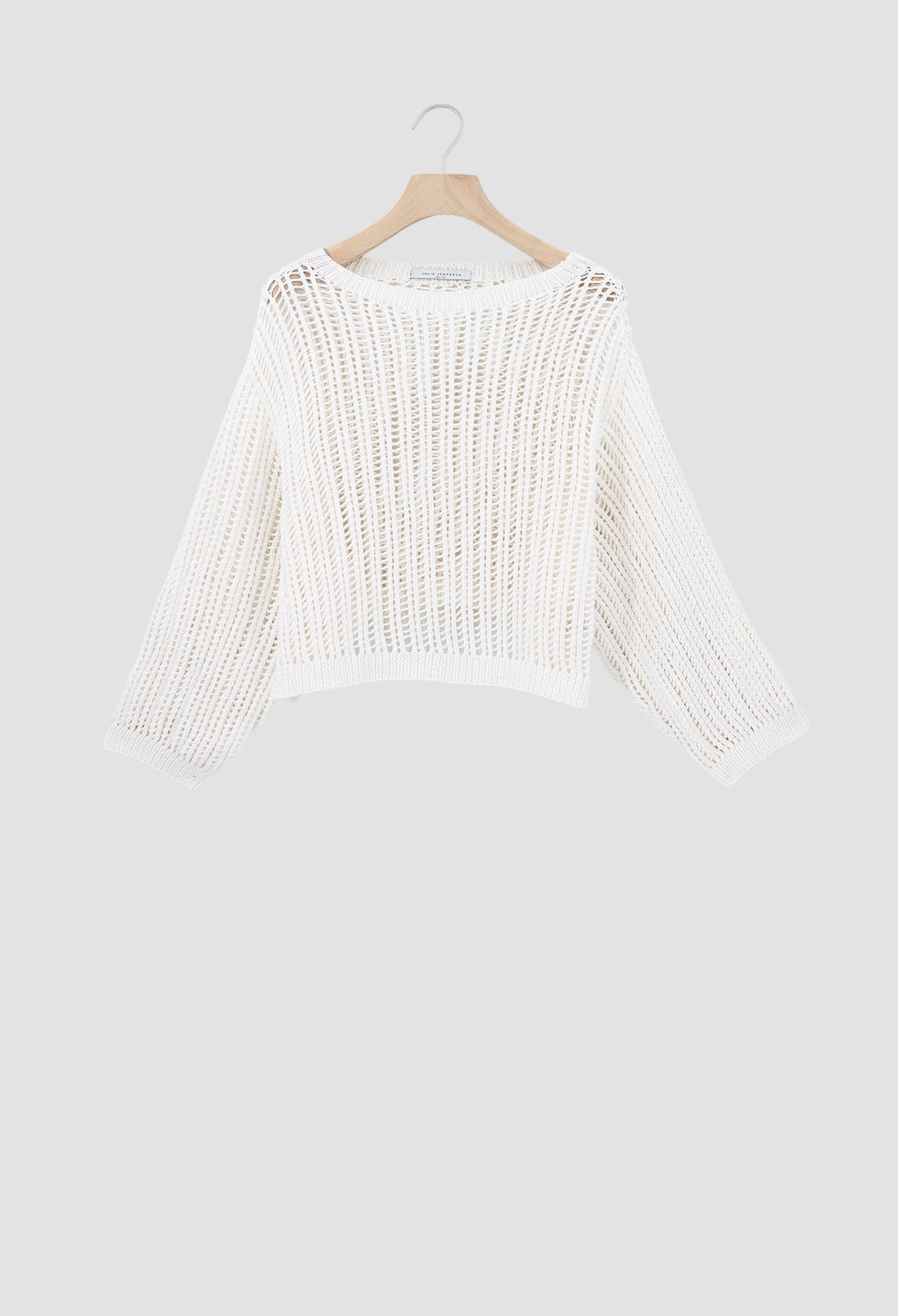 An off-white open-knit cropped sweater with three-quarter sleeves, hanging on a wooden hanger against a light gray background.
