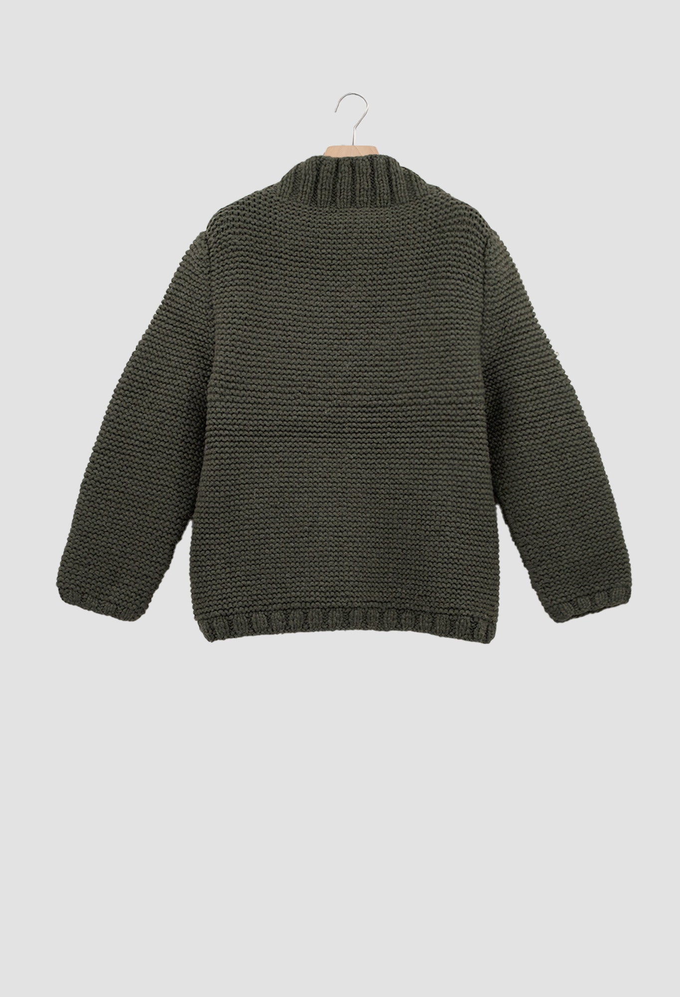 Green knitted sweater on a hanger against a light gray background