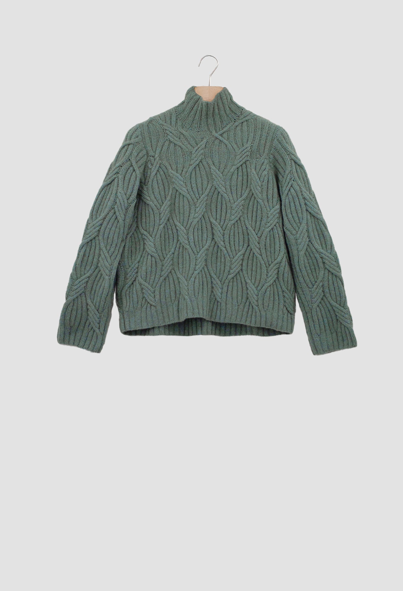 Green cable knit sweater on a hanger against a light gray background
