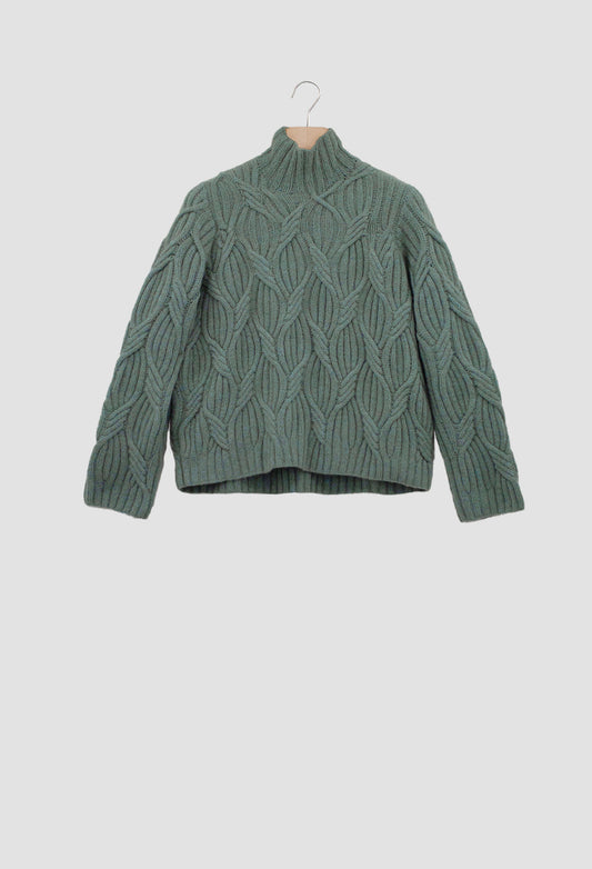 Green cable knit sweater on a hanger against a light gray background