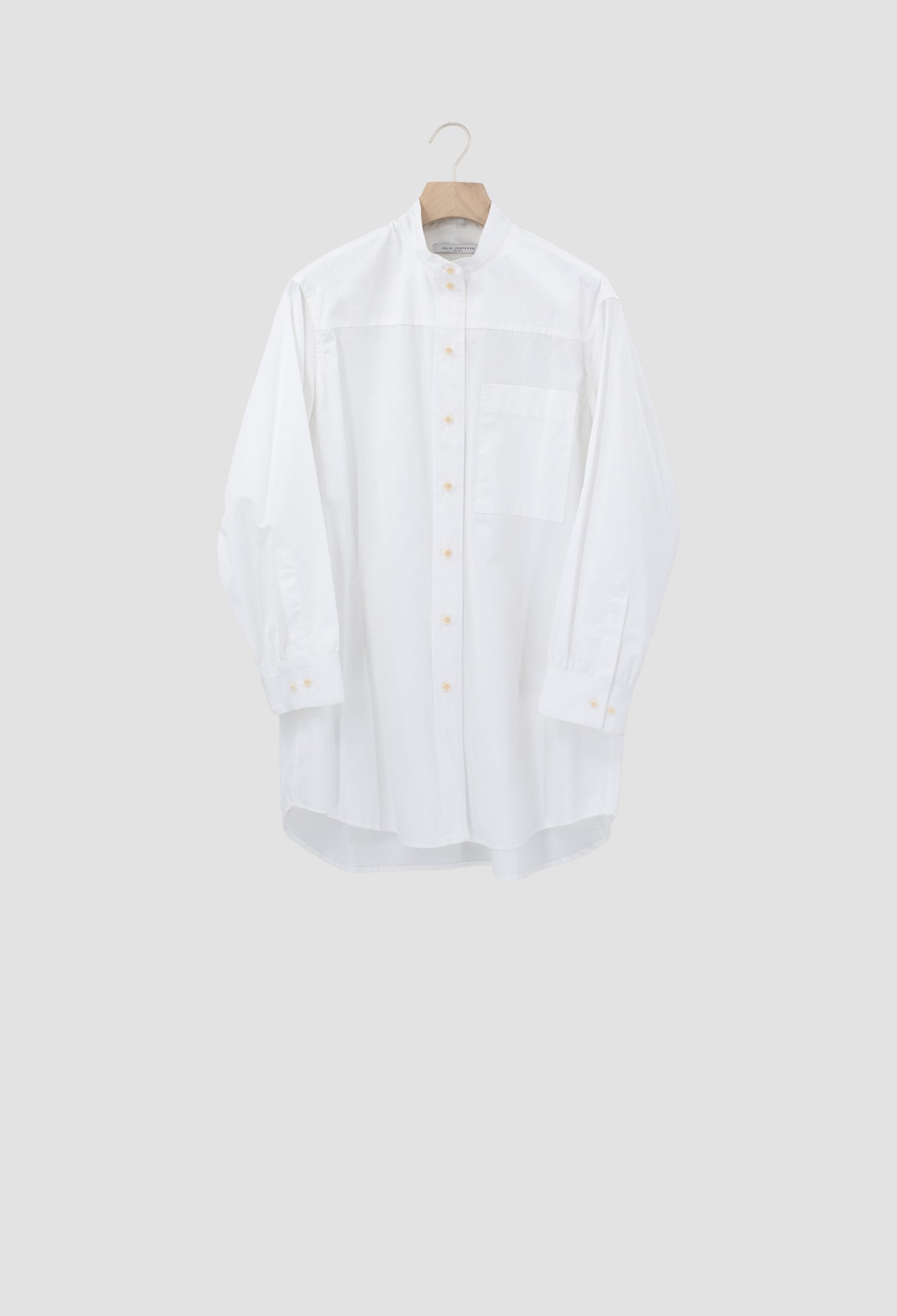 A white long-sleeve button-up shirt with a band collar, displayed on a wooden hanger against a light gray background.