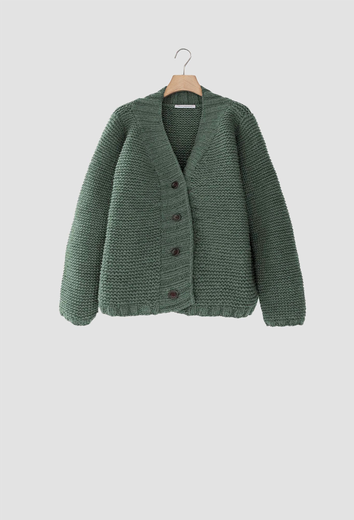 Green knitted cardigan on a hanger against a light gray background