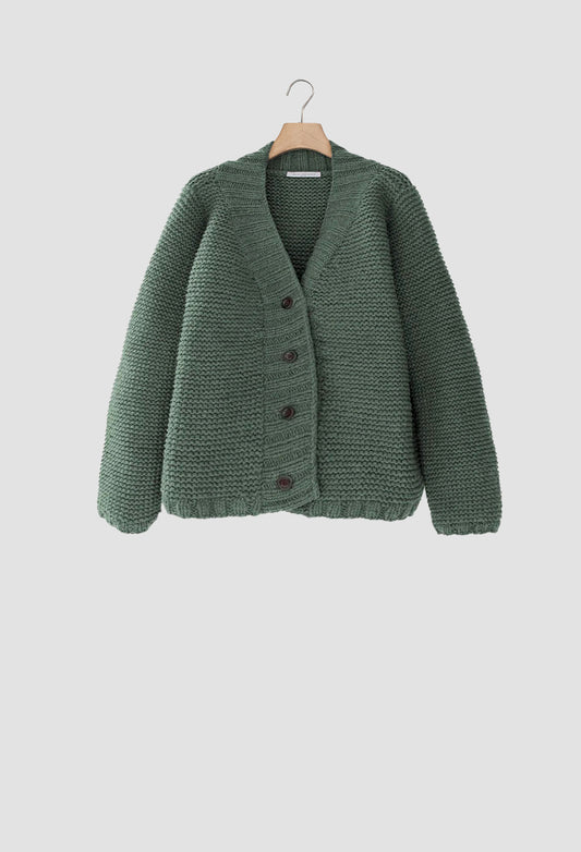 Green knitted cardigan on a hanger against a light gray background