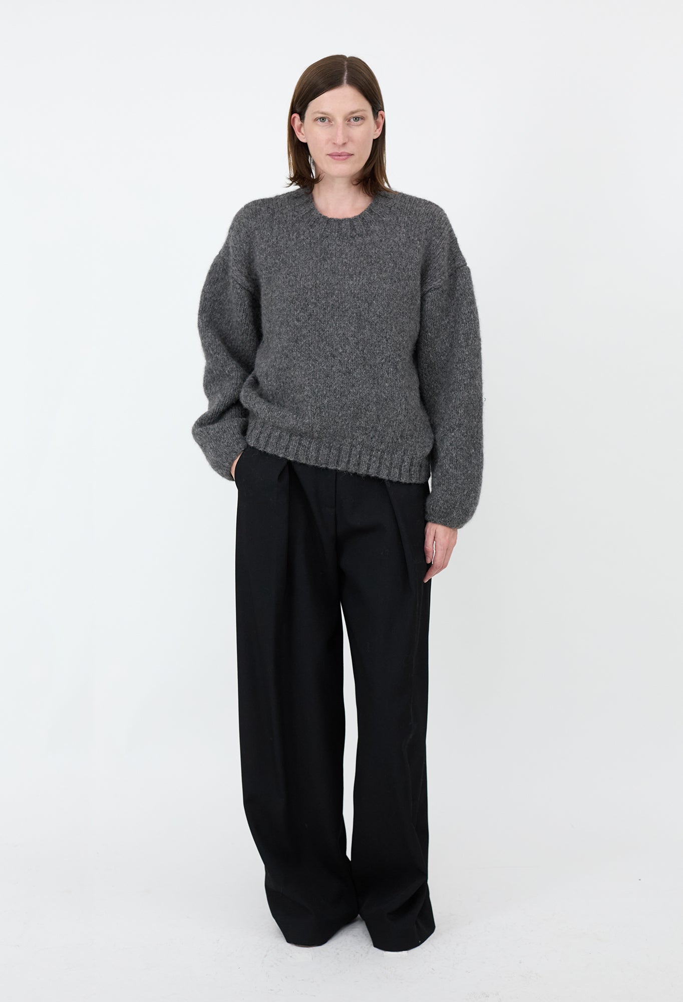 Person wearing a gray sweater and black pants on a white background