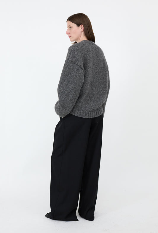 Person wearing a gray sweater and black pants on a white background