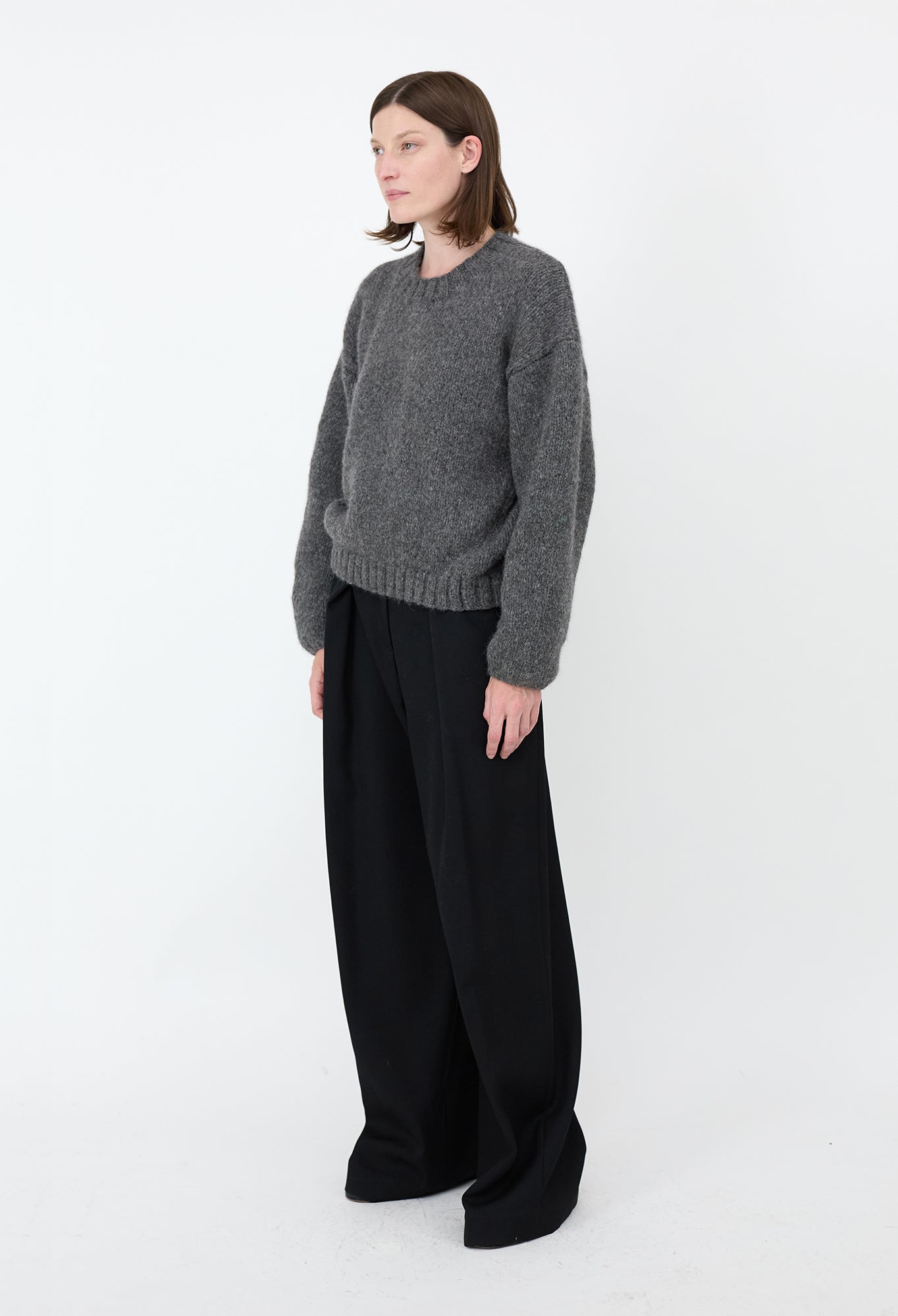 Woman wearing a gray sweater and black pants on a white background