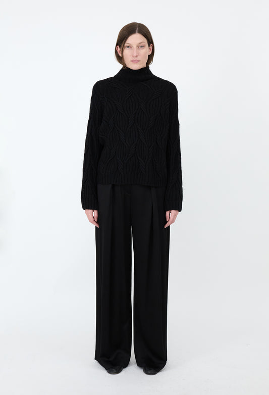 Person wearing a black turtleneck and wide-leg pants on a white background