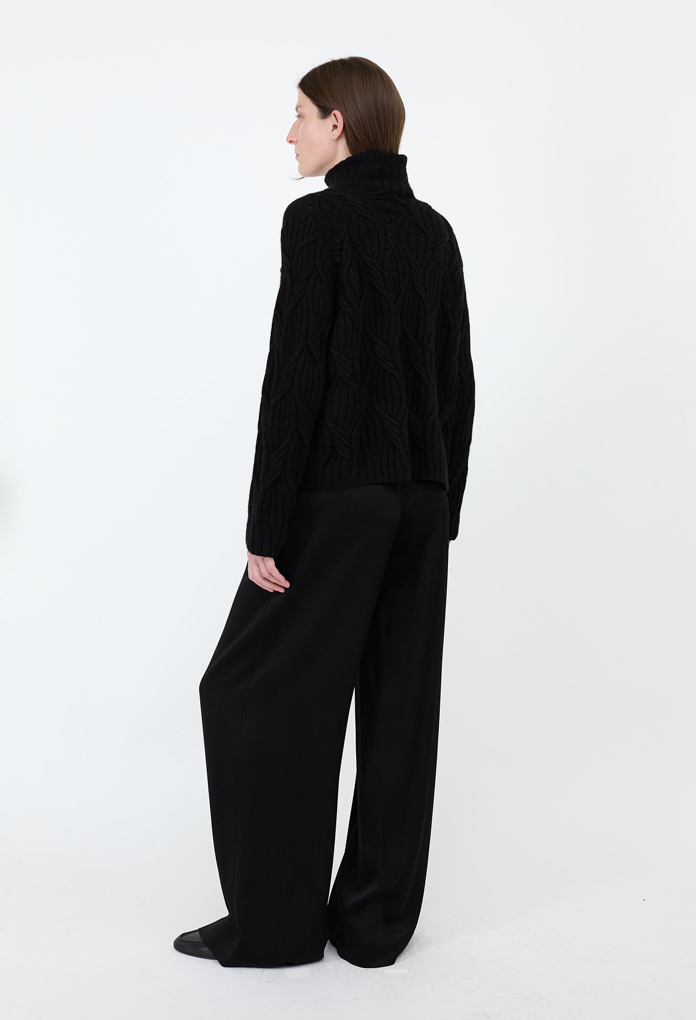 Person wearing a black turtleneck sweater and wide-leg pants on a white background