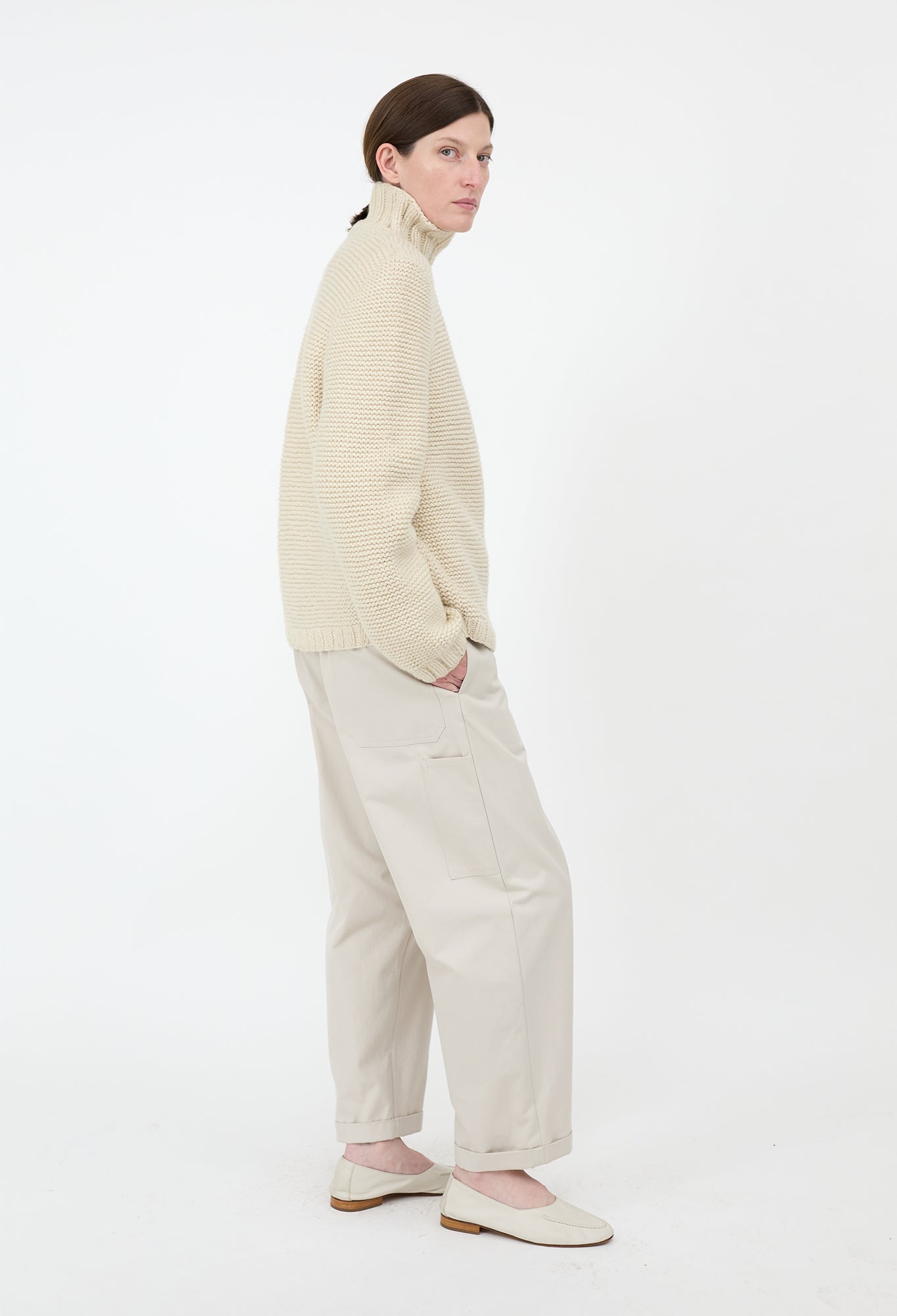 Person wearing a beige sweater and pants on a white background