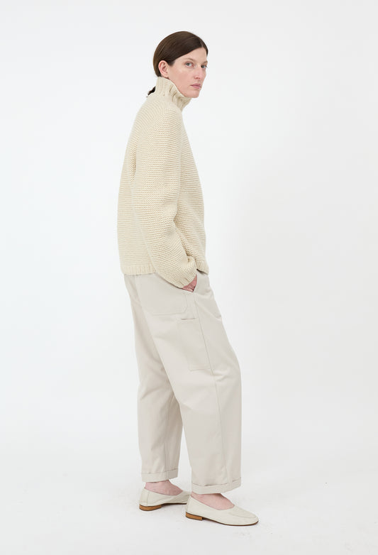 Person wearing a beige sweater and pants on a white background