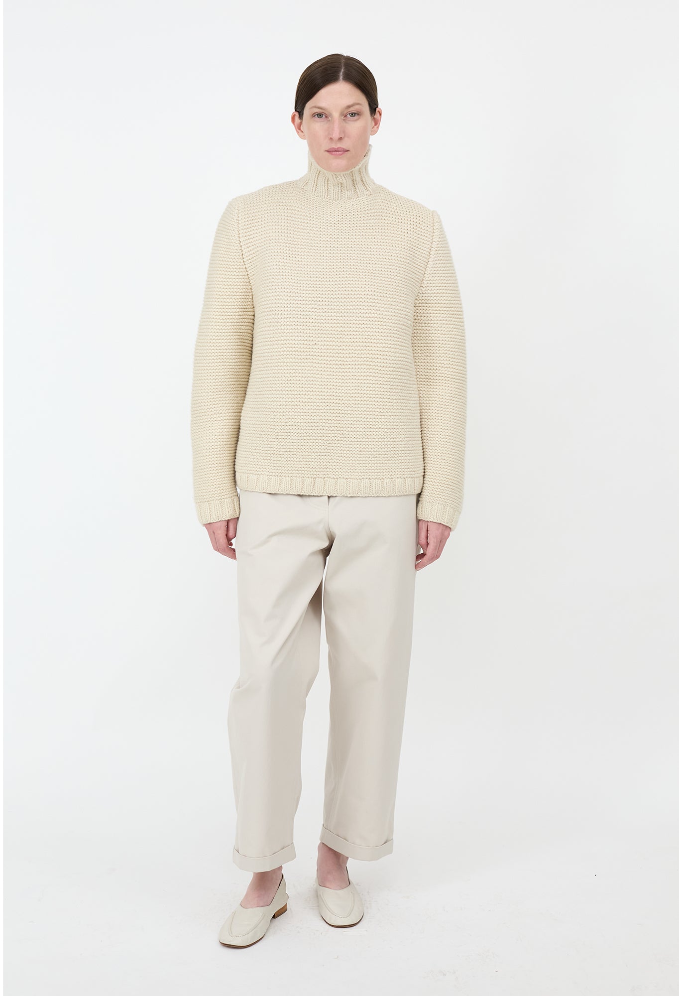 Person wearing a beige sweater and pants on a white background