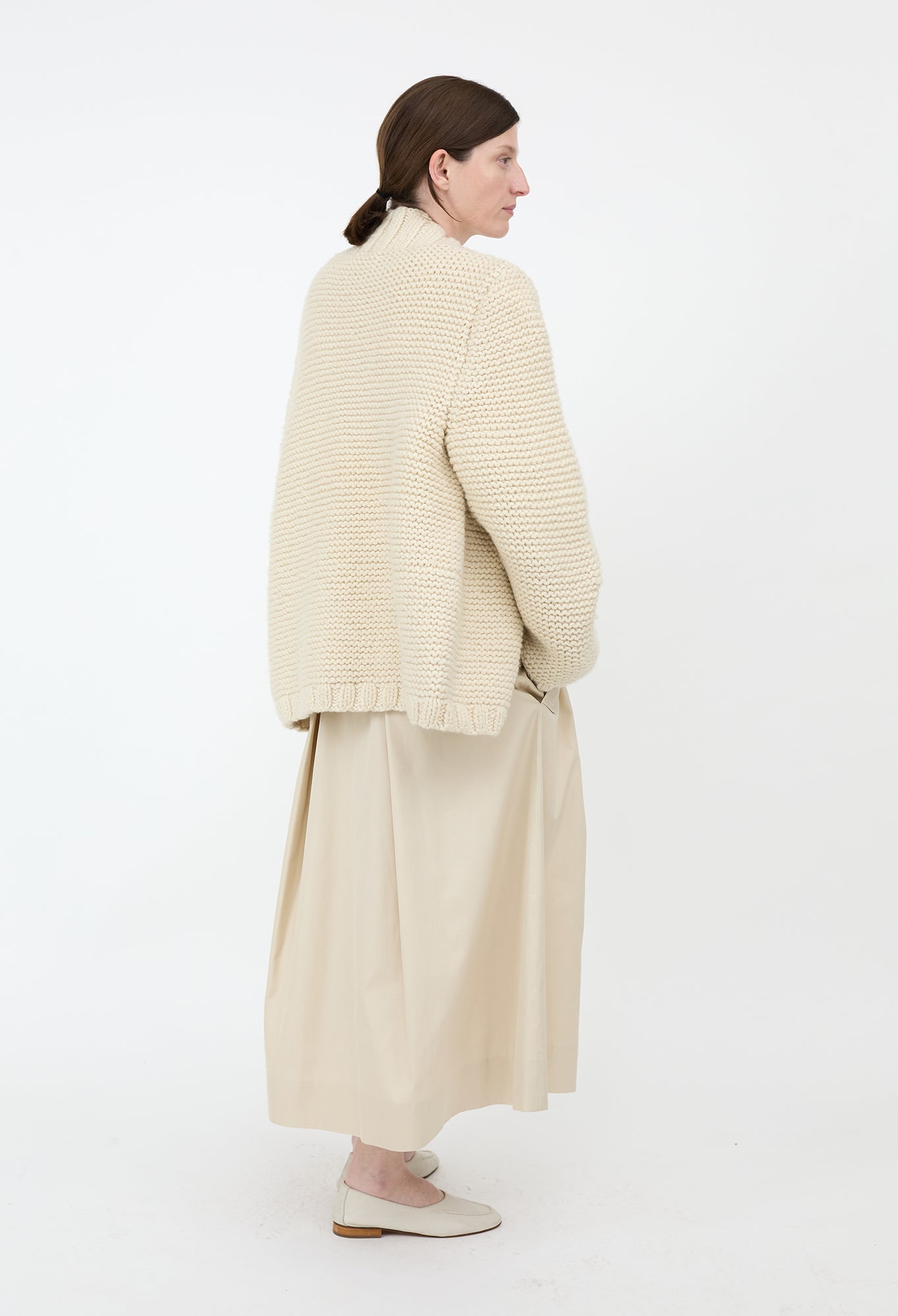 Person wearing a beige knitted cardigan and skirt on a white background